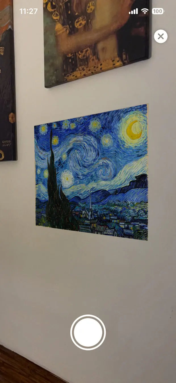 Augmented reality view: Van Gogh&rsquo;s Starry Night shown as a printed poster hanging flat on a pale wall, next to two real framed canvases.