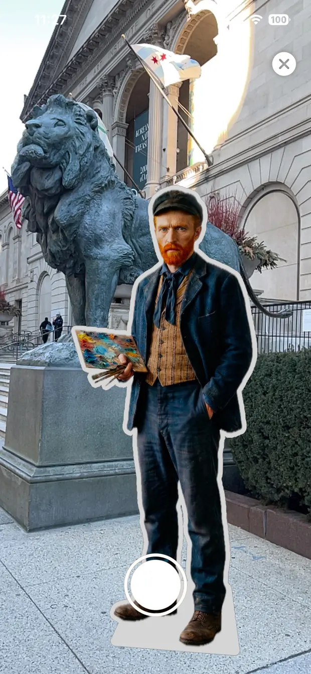 Augmented reality view: a life-size cutout of a man holding a paint palette standing on the pavement outside the Art Institute of Chicago, beside one of the bronze lions.